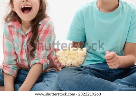 Details on a bowl of popcorn in the hands of cute cheery children watching movies or cartoons over white isolated background. People. Kids. Childhood. Lifestyle. Leisure activity. Entertainment