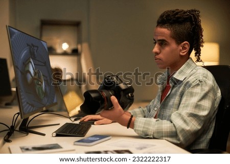 Young photographer sitting at his workplace with camera and retouching photo on computer