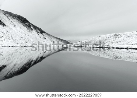 Black and white winter picture of Bowscale Tarn in the English Lake District with snow, calm water and reflections.