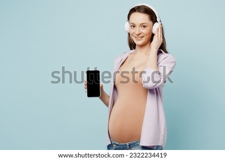 Young pregnant mom woman with belly tummy with baby wearing casual clothes headphones listen to music use blank screen mobile cell phone isolated on plain blue background. Maternity pregnancy concept