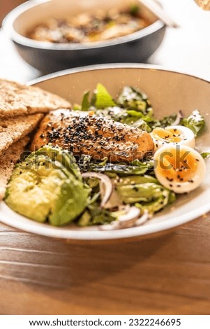 Fresh leaf salad served with avocado, eggs and grilled salmon on the top studded by sesame.