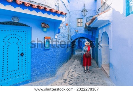 Colorful traveling by Morocco. Young woman in red dress walking in medina of blue city Chefchaouen.