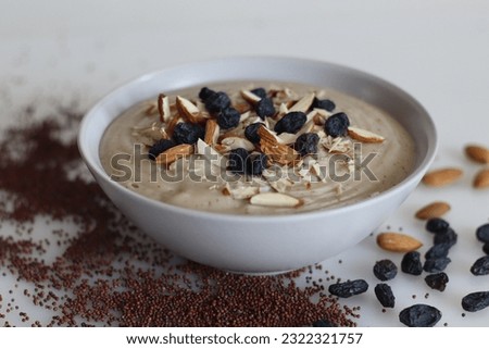 Ragi porridge. A porridge made of finger millet flour, sweetened with jaggery and served with sliced and crushed almonds and raisins. A healthy breakfast. Shot on white background Royalty-Free Stock Photo #2322321757