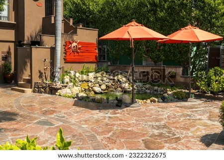 a patio with a koi pond surrounded by rocks, orange umbrellas and lush green trees and plants in Long Beach California USA