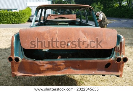 Back of a totally rusted old car with a man in the background photographing it