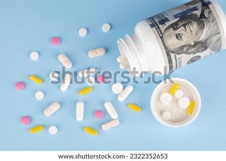 Dollars and pills spilling out of pill bottle on blue background. The concept of expensive medicine.