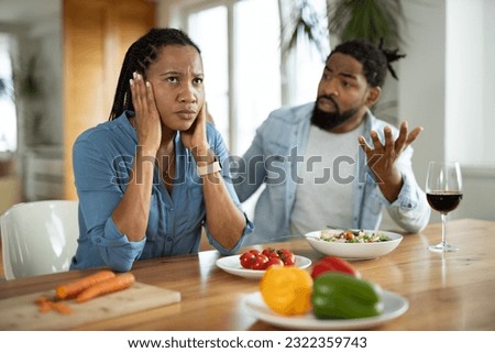 Angry black man shouting at his wife  during their breakfast at dining table  while she is covering her ears
