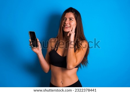 Image of a thinking dreaming Young beautiful brunette woman wearing sportswear using mobile phone and holding hand on face. Taking decisions and social media concept.
