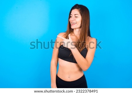 Happy cheerful smiling Young beautiful brunette woman wearing sportswear looking and pointing aside with hand. Copy space and advertisement concept.