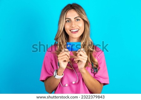 Photo of young beautiful doctor woman standing over blue studio background positive smile hold credit card income salary