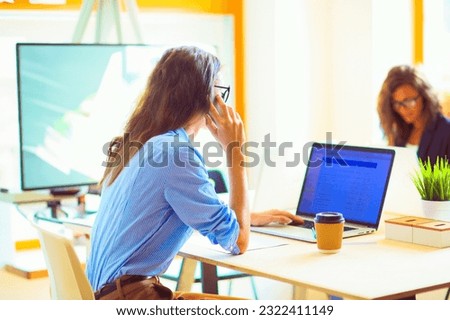 Beautiful young business woman sitting at office desk and talking on cell phone. Business woman