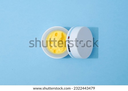 Beauty product photo of a yellow face cream on a blue background