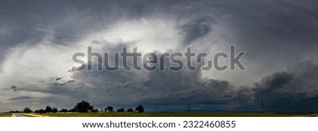 Panoramic view of severe thunderstorm moving across country with gray overcast sky and fields in foreground