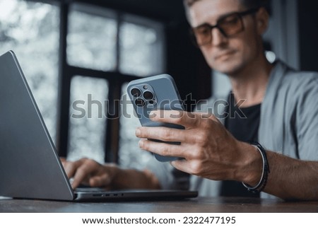 Young beard man using laptop on office, freelance work, outdoor close up hipster portrait, brutal, guy listening music on earphones, make photo and video, production, Bali, coffee cup, smartphone Royalty-Free Stock Photo #2322477195