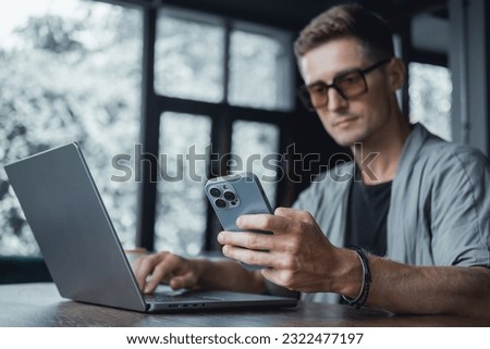 Pretty Young Handsome Man Using Laptop in cafe, outdoor portrait business man, hipster style, internet, smartphone, office, Bali Indonesia, holding, mac OS, manager, freelancer , watch, cappuccino Royalty-Free Stock Photo #2322477197