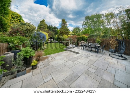 Beautiful summer garden in England, UK with lawn and large, indian sandstone patio. Royalty-Free Stock Photo #2322484239