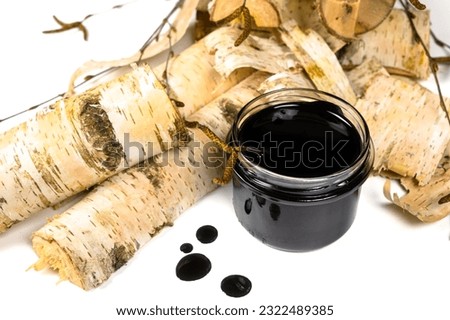 Birch tar or pitch in a jar and birch tree bark on white background. Wood tar. Liquid mineral tar from birch bark Royalty-Free Stock Photo #2322489385