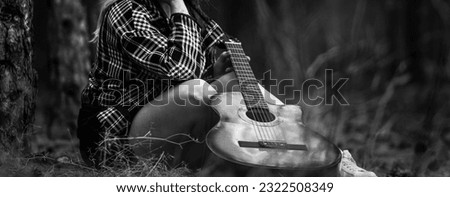 Girl  sitting on the ground with guitar in the forest. 