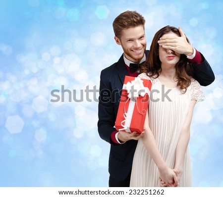 Making a surprise man covers eyes of his pretty girlfriend, blue light background