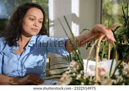 Inspired female florist, gardener floriculturist in casual shirt, a seller in flower shop holding wicker basket with flower composition for Wedding Day, Women's or Mother's Day. People. Small business Royalty-Free Stock Photo #2322514975