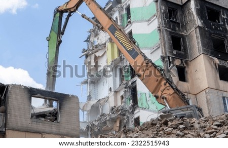 Facade of a residential abandoned multi-storey building after a strong fire. A construction excavator with a hydraulic crusher demolishes a house for repairs. The collapse of a residential building Royalty-Free Stock Photo #2322515943