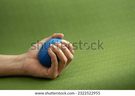Hands of a man squeezing a blue stress ball on the yoga mat Royalty-Free Stock Photo #2322522955