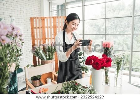 Beautiful florist taking pictures of beautifully arranged vase flowers with bright face in flower shop to promote the store.