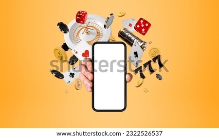 Man hand showing a smartphone mock up blank screen, roulette and casino poker cards with money falling on orange background. Concept of online game, mobile app and gambling Royalty-Free Stock Photo #2322526537