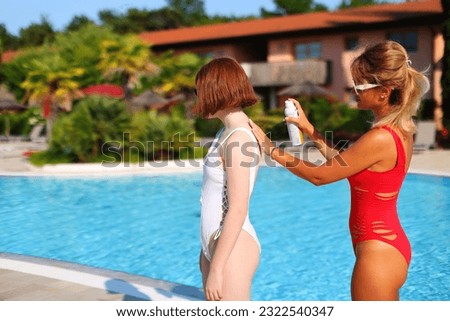 Top view of a girl smearing sunscreen on the back of her friend. white and red bathing suit