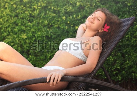 girl sunbathes and relax in deck chair, woman rest by the swimming pool near green background, in the yard of her house or hotel in summer
