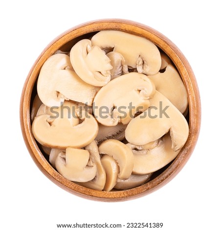 Canned sliced white champignon mushrooms, in a wooden bowl. Agaricus bisporus, also called common, button, cultivated or table mushroom. Close-up from above, isolated on white background, food photo. Royalty-Free Stock Photo #2322541389