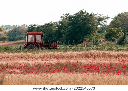 A picturesque scene with a tractor on a dirt road, surrounded by a wheat field adorned with poppies, and a backdrop of a forest.