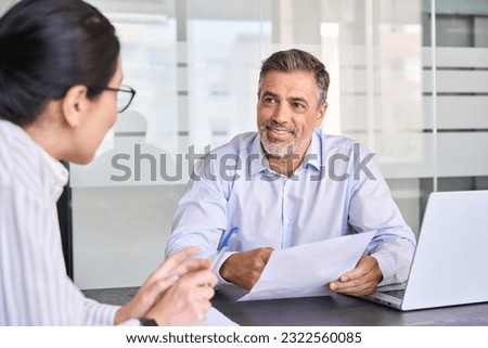 Smiling professional Latin employer hr manager holding cv during interview hiring for job female Asian female recruit, advisor consulting client sitting in office at meeting. Human resources. Royalty-Free Stock Photo #2322560085
