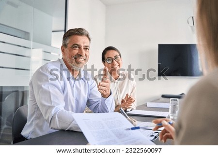 Smiling Latin manager working with diverse colleagues at team meeting. Happy diverse business people international corporate executives talking at group briefing, collaborating at boardroom table. Royalty-Free Stock Photo #2322560097