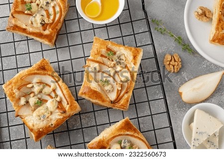 Mini tarts with puff pastry, pieces of pear, blue cheese, walnuts and honey on a concrete background. Top view Royalty-Free Stock Photo #2322560673