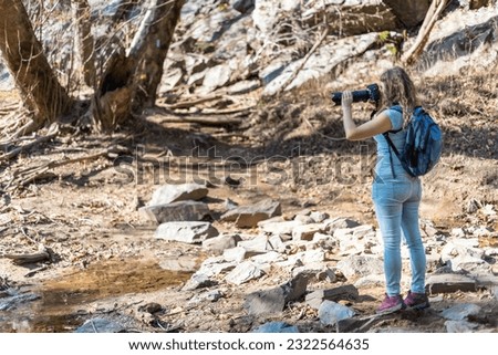 Young woman photographer with backpack and camera taking photo photographing Great Falls in autumn in Maryland