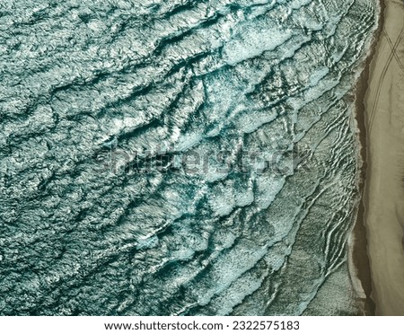 Aerial photography shoot from a small aircraft over a sandy beach with textured waves and car tracks on the sand on Moreton Island in Queensland, Australia. 