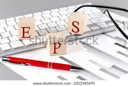 EPS written on wooden cube on the keyboard with chart on grey background