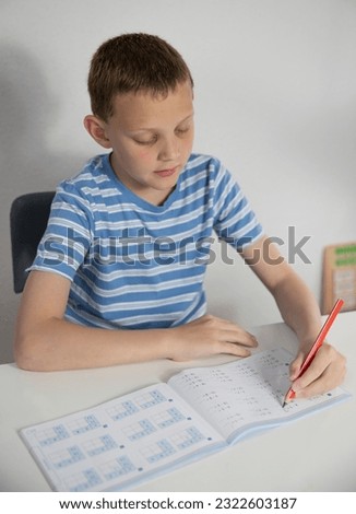 A boy of 9 years old sits at a table and does homework for school and math
