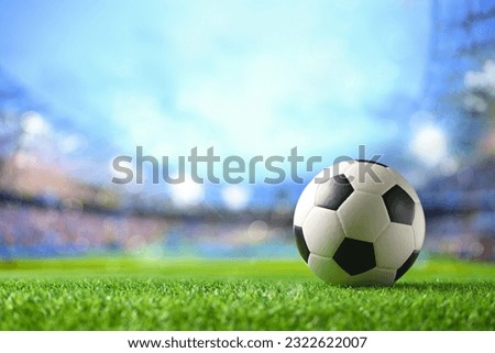 Close-up football ball on grass with football stadium background.