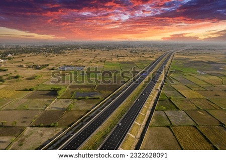 locked tripod aerial drone shot of new delhi mumbai jaipur express elevated highway showing six lane road with green feilds with rectangular farms on the sides Royalty-Free Stock Photo #2322628091