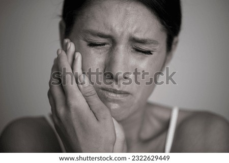 Toothache. Girl suffering from toothache and cheek touch while sitting on sofa at home. Dental problem concept. Stock photo