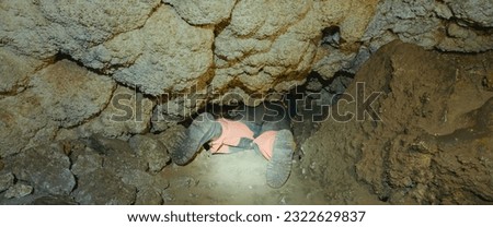 The cave explorer embark on a dangerous adventure as one squeezes through a narrow, horrifying crevice crawling on their belly under the rock. Enclosed space evokes fear panic on this extreme journey Royalty-Free Stock Photo #2322629837