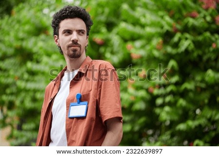 Smiling software developer with badge on shirt standing outdoors and looking away Royalty-Free Stock Photo #2322639897