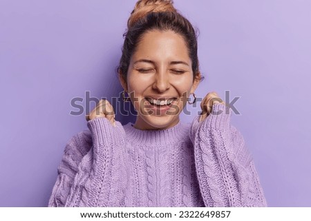 The woman outfit adds to her warmth. She is dressed in a cozy knitted jumper which enhances the sense of comfort. Vibrant purple background further intensifies atmosphere of celebration and success. Royalty-Free Stock Photo #2322649857