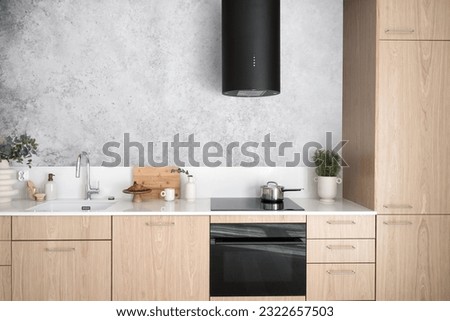 modern interior in kitchen room, wood cabinet with white countertop, glass ceramic hob, sink with water tap and hood extractor against grey wall Royalty-Free Stock Photo #2322657503