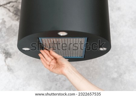 Woman removing filter from cooker hood for cleaning or service. Process of replacing dirty elements in kitchen extractor fan. Modern appliance for air purification during cooking food in apartment Royalty-Free Stock Photo #2322657535