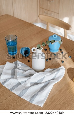 composition of cotton dish towel, ceramic vase with eucalyptus branch, glass of water and fresh blueberry on wooden tabletop, high angle shot Royalty-Free Stock Photo #2322660409