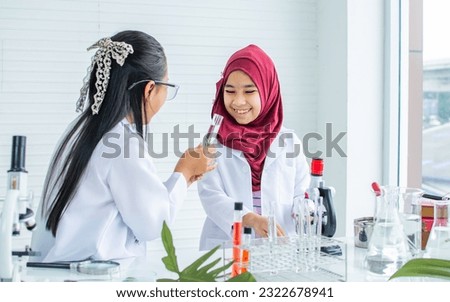 Two diverse multiethnic little girls wearing white ground uniform, hijab, headscarf, studying science in classroom at school, using stethoscope for research plants, happily smiling. Education Concept