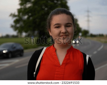 A girl in a red blouse and a black jacket close-up portrait of her smiling. Behind сountry road on which cars pass late at night